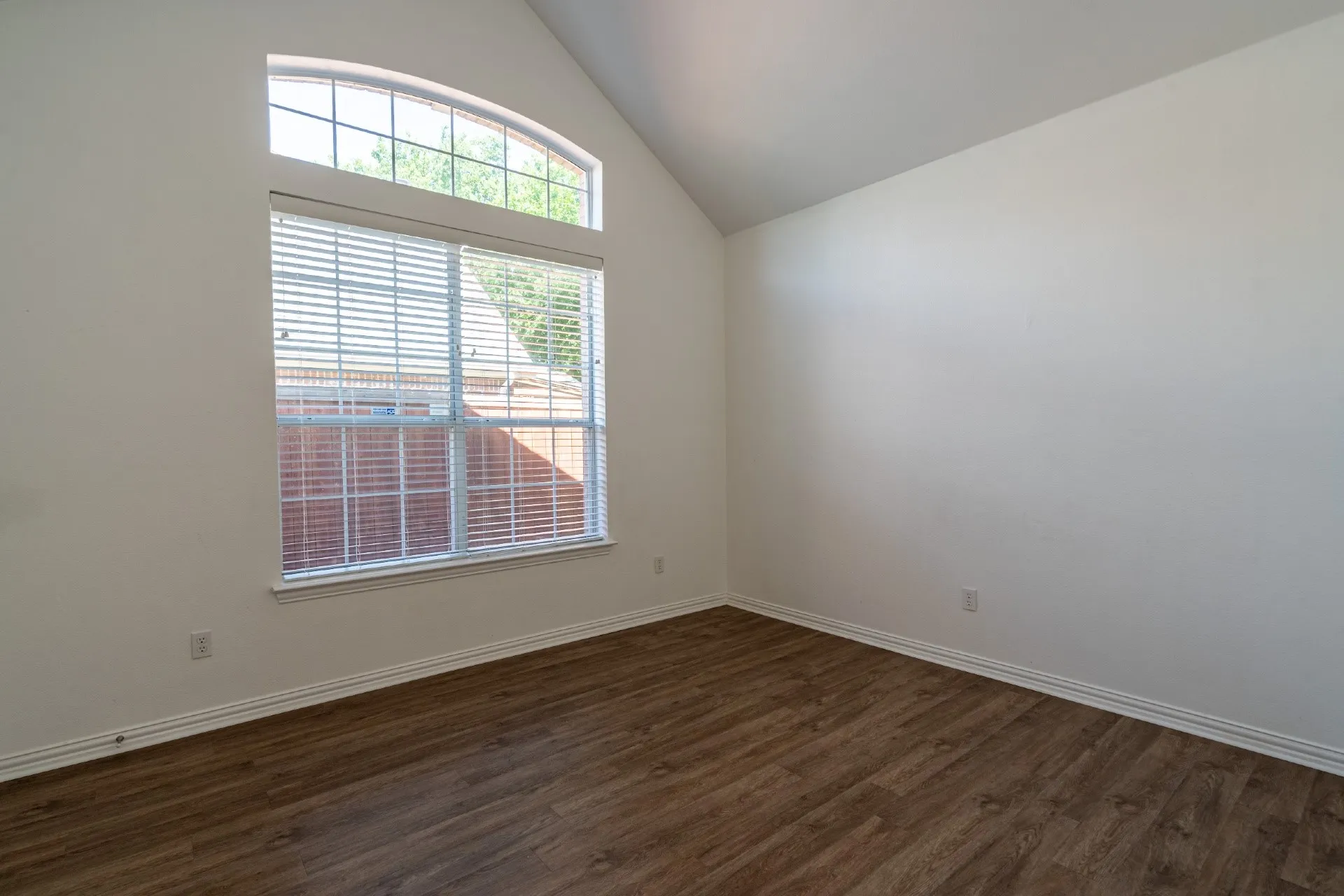 Vaulted ceiling, arched transom window, wood-finish flooring, white walls, and white window blinds