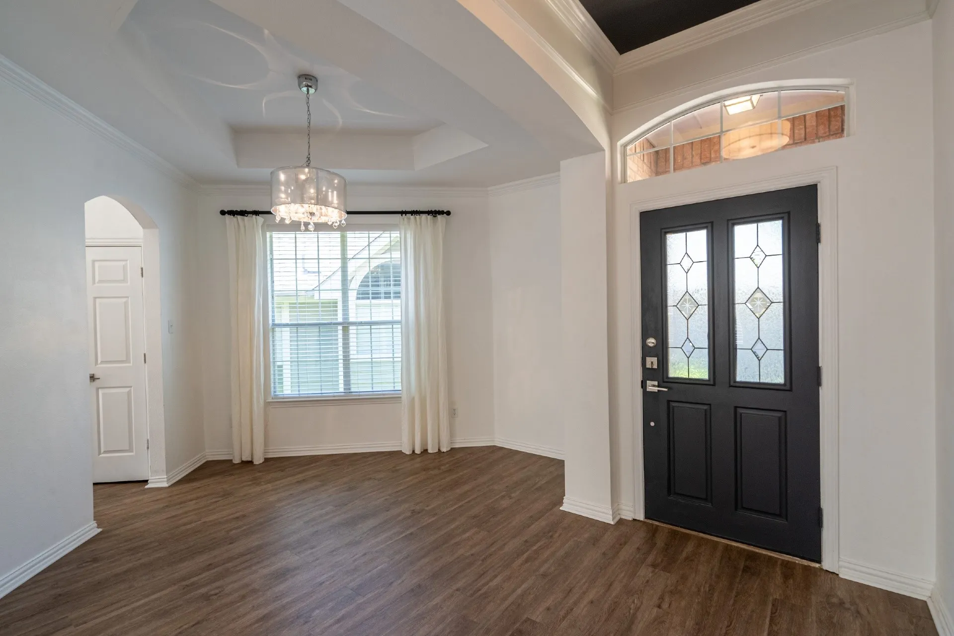 Wood-finish flooring, recessed ceiling with a decorative light fixture, arched doorway, and an entry door with decorative glass inserts
