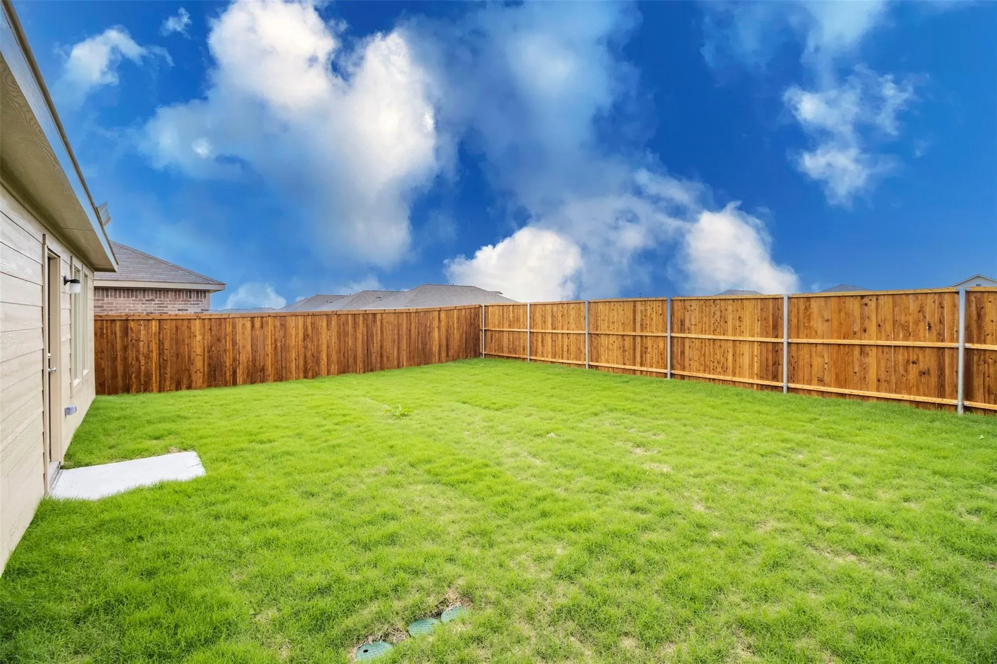 Expansive green lawn with a wood plank privacy fence and tan siding