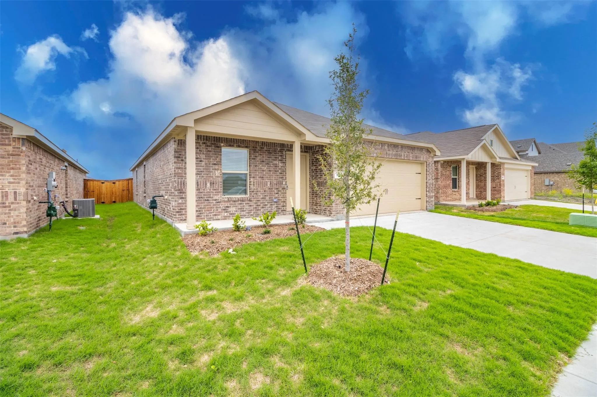 Brick exterior with a gabled roofline, concrete driveway, attached garage, and landscaped front yard