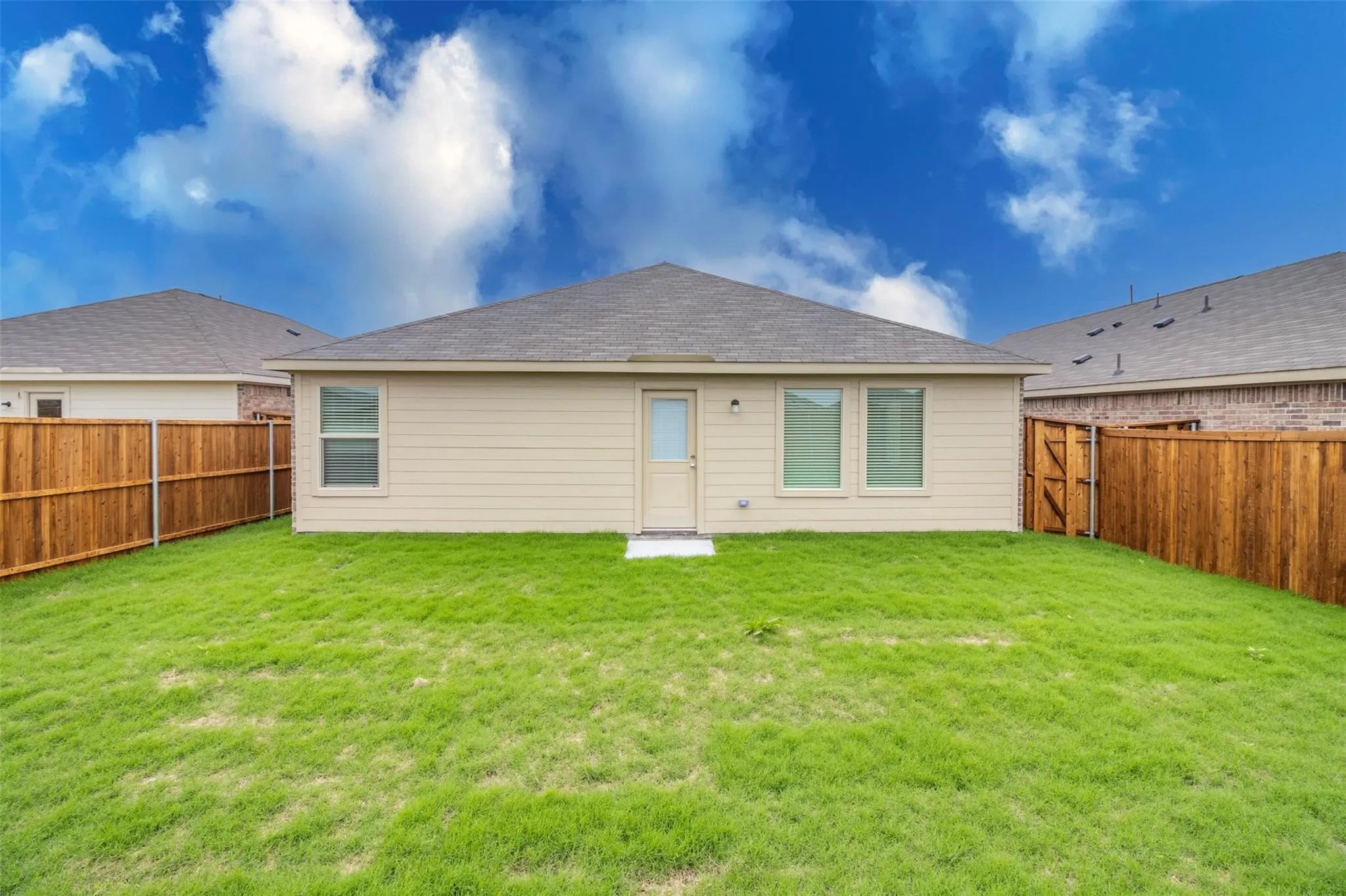 Expansive backyard with a manicured lawn, full privacy fencing, and a rear exterior door