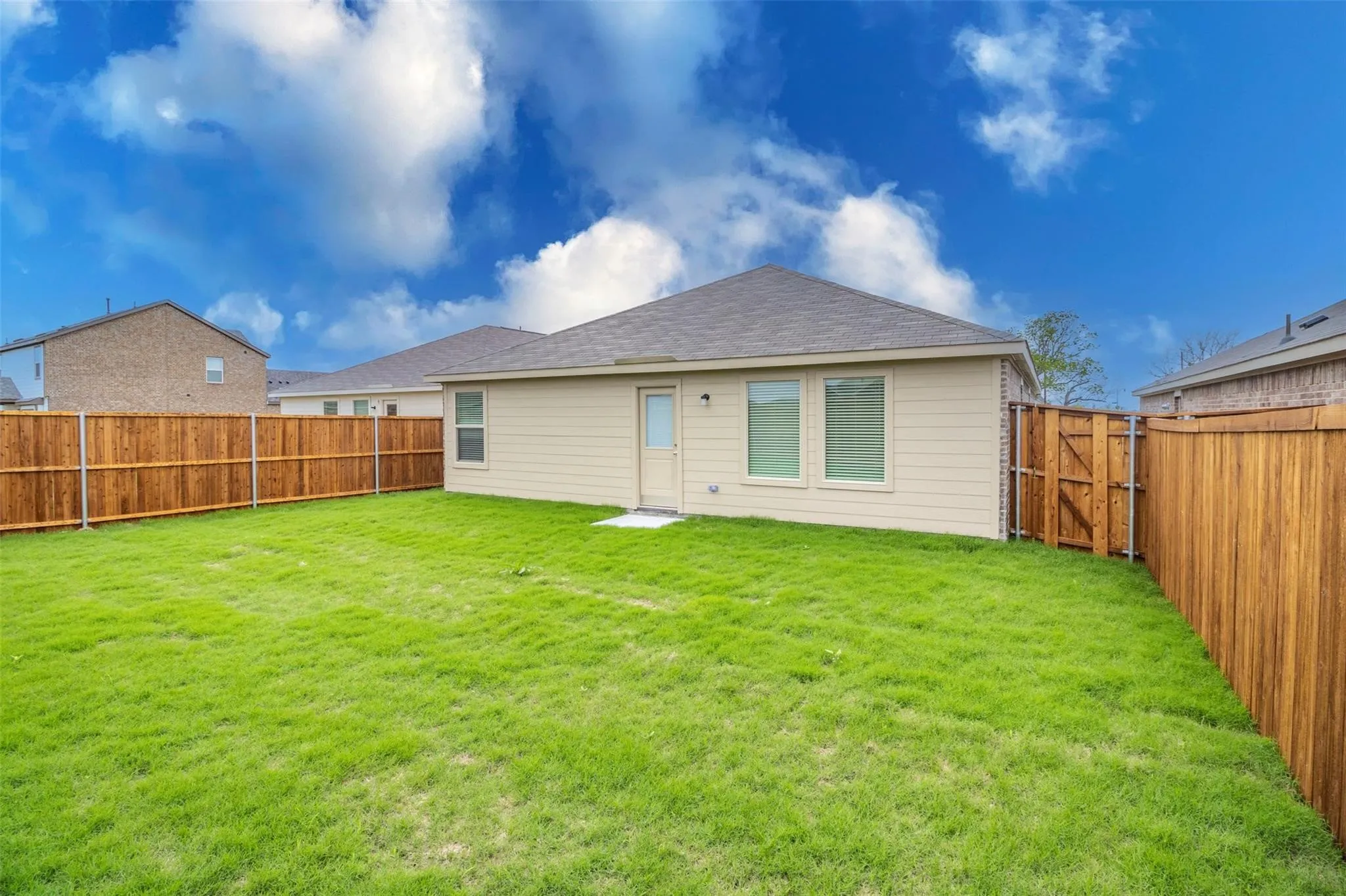 Expansive grassy yard with wood fencing, a beige exterior, and a dark shingle roof