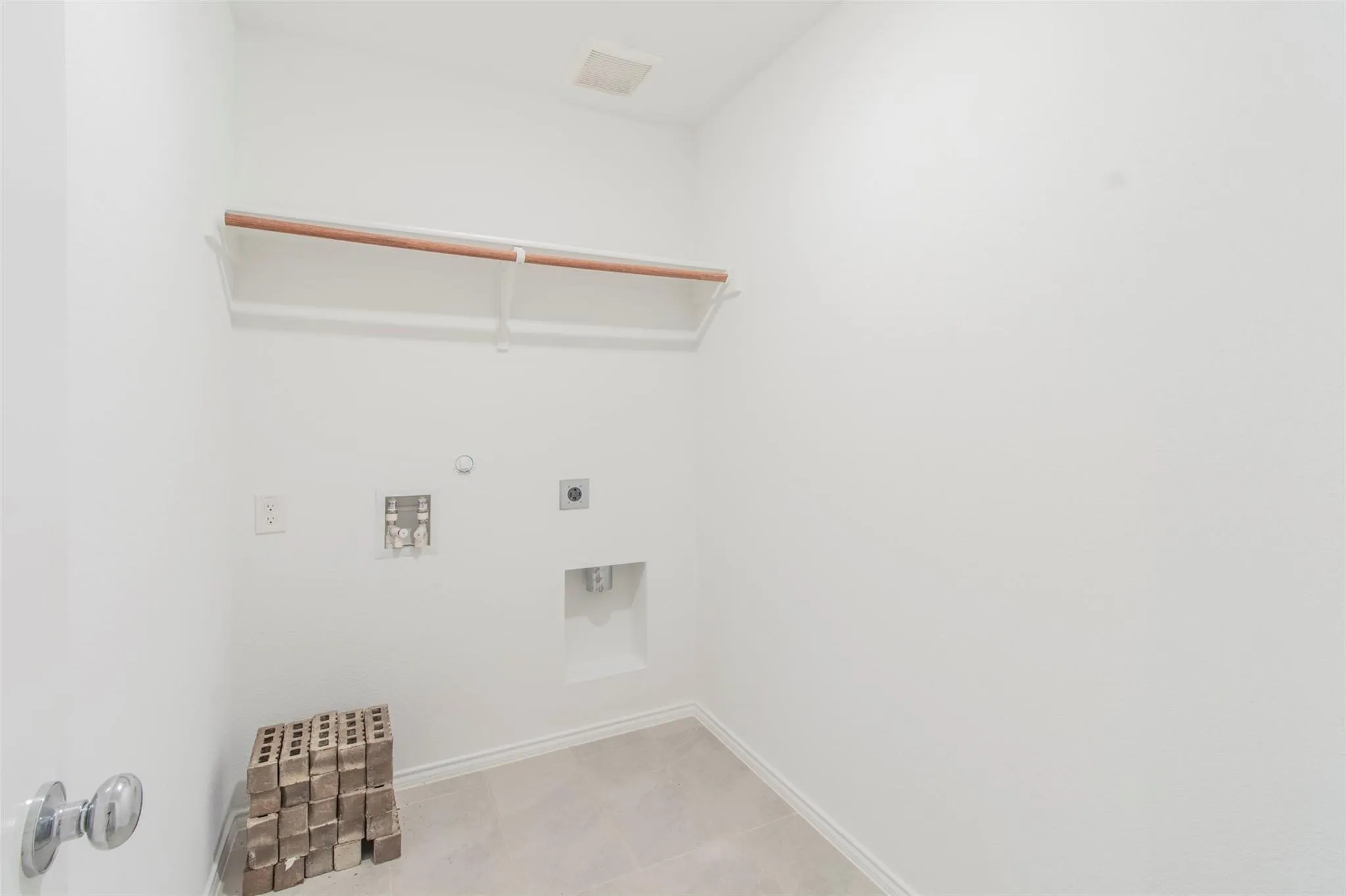 Utility space with light gray floor tile, white walls, built-in shelving, and laundry hookups
