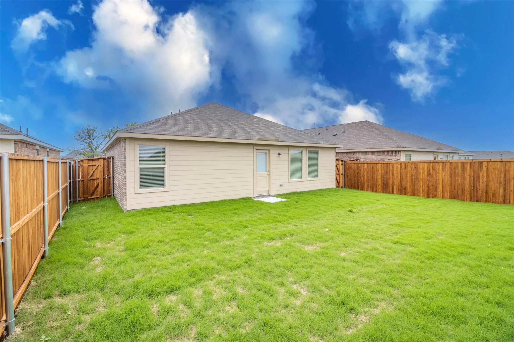 Expansive backyard featuring a manicured lawn, full wood fencing, and a side access gate