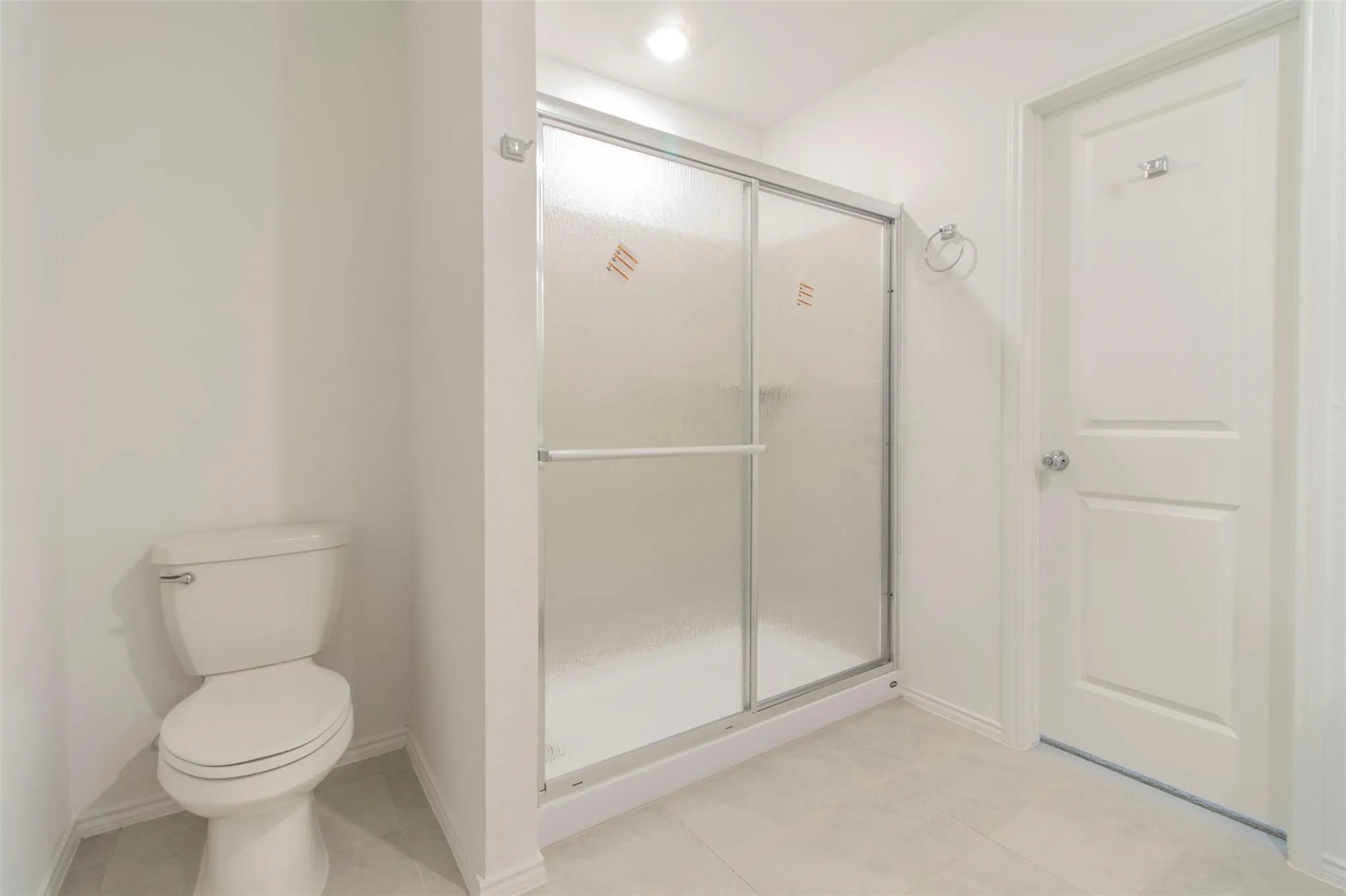 White toilet fixture, framed shower enclosure with sliding frosted glass doors, and light-toned floor tile