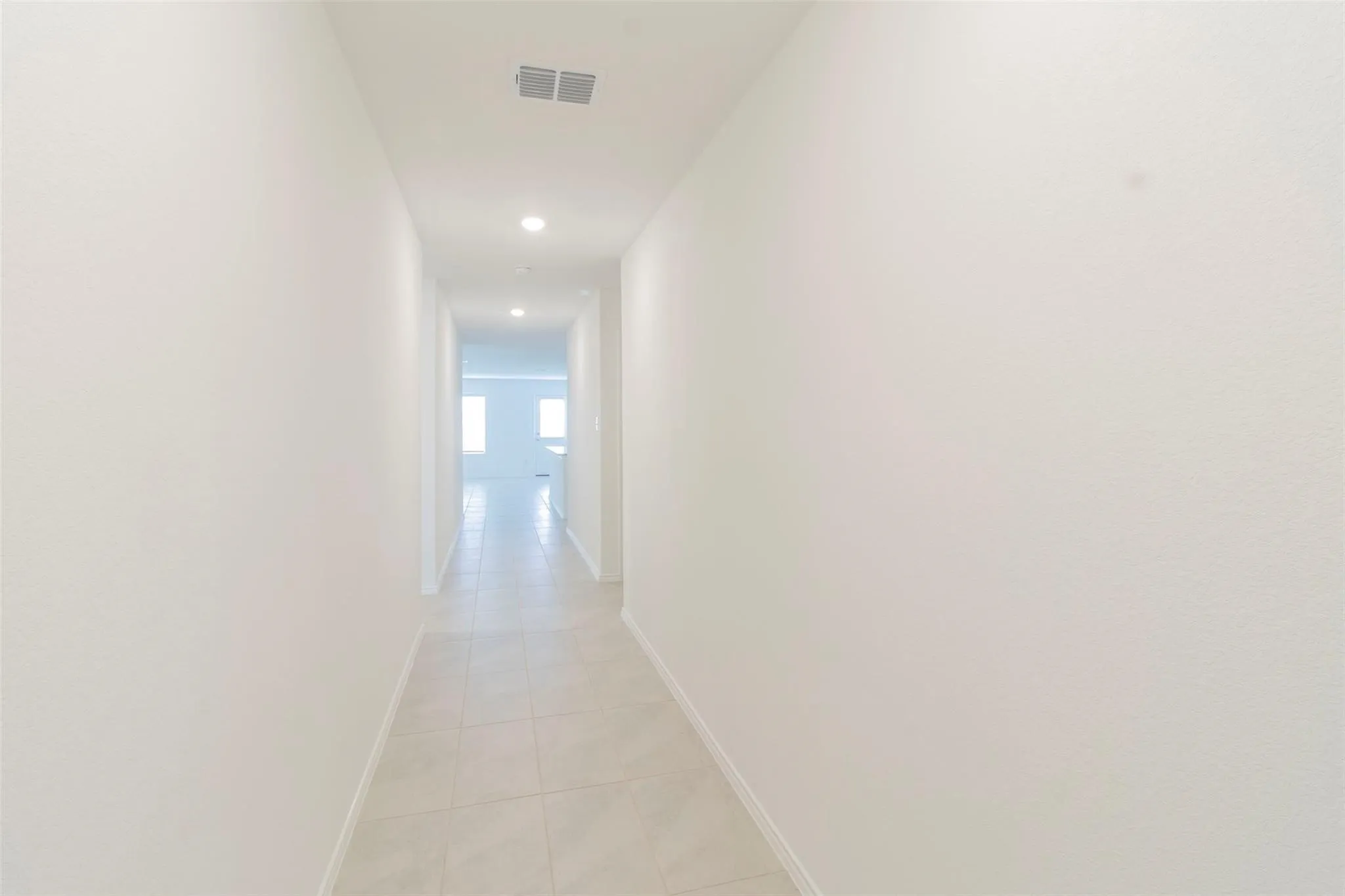 Recessed lighting illuminates a hallway with light-toned tile flooring and white wall finishes