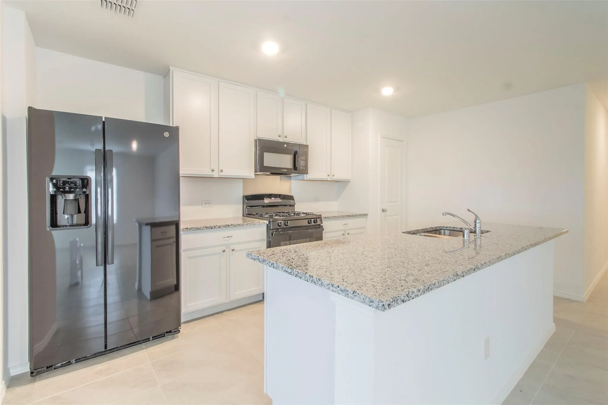 Kitchen featuring a granite island, stainless steel sink, white cabinetry, black appliances, and light tile flooring