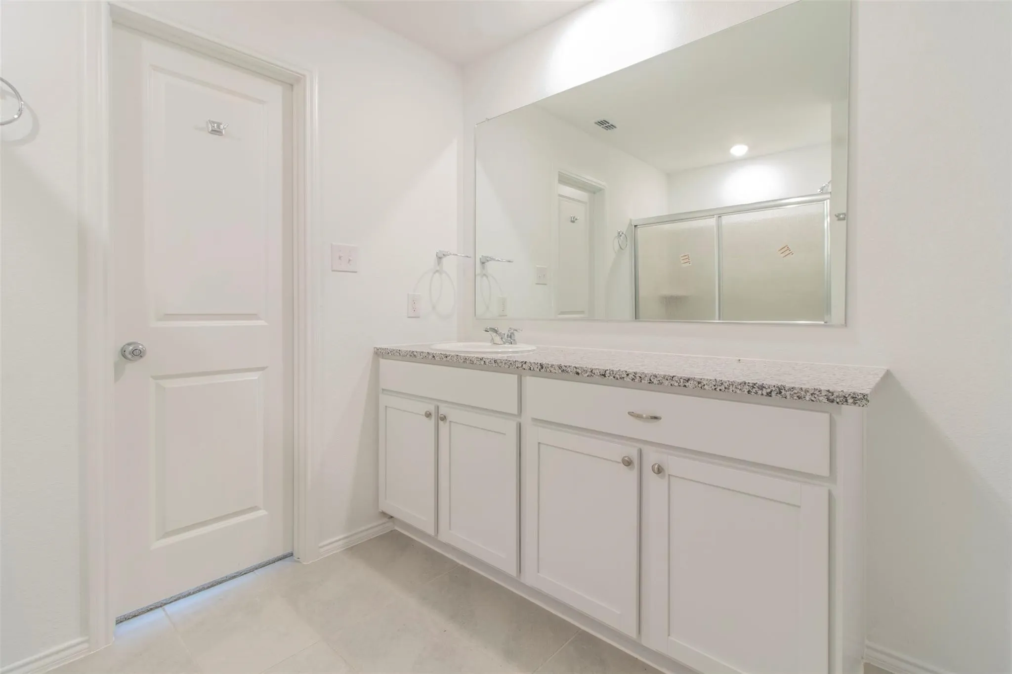 White panel door, white vanity cabinetry, speckled countertop, recessed lighting, and a large wall-mounted mirror