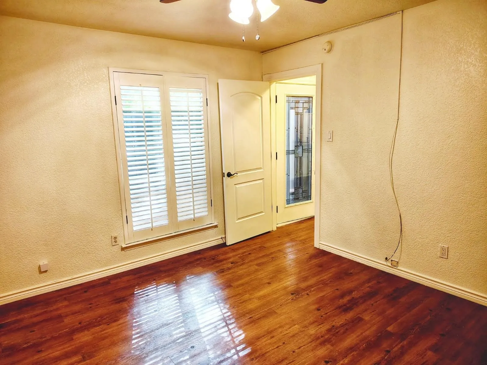 1st floor bedroom, Wood-finish flooring throughout, white plantation shutters, white interior door, and ceiling fan with integrated lighting