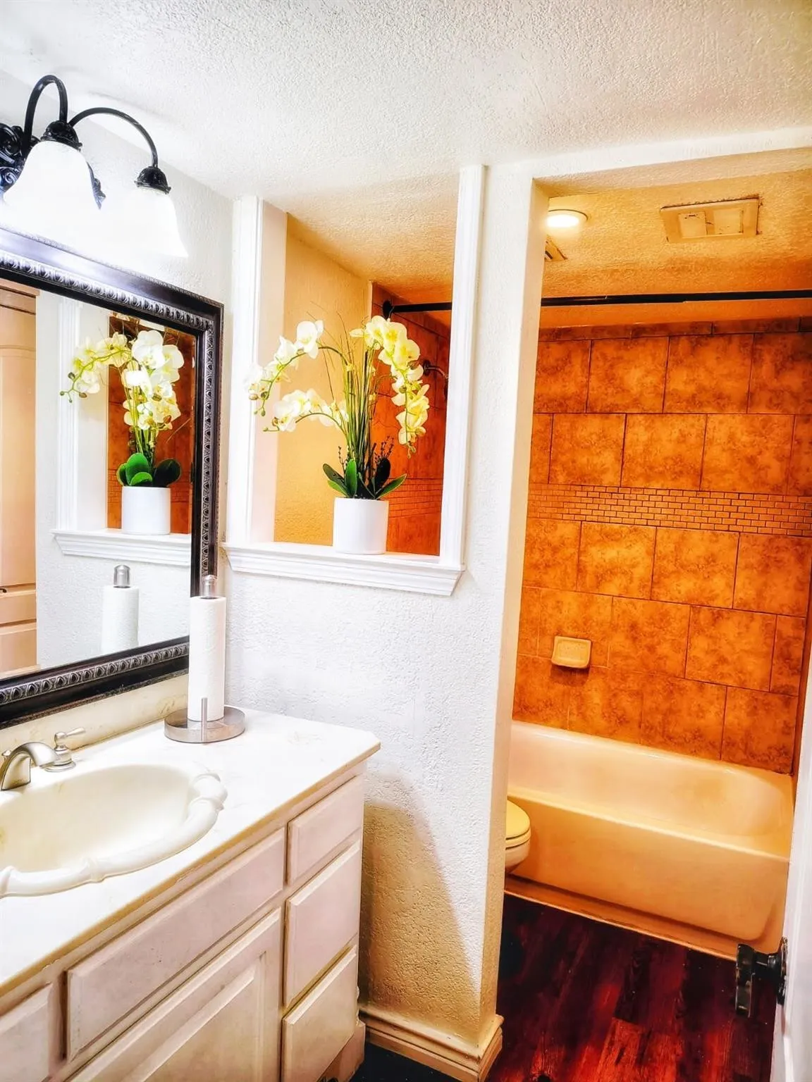 Built-in vanity with integrated sink, wall-mounted light fixture, and framed mirror