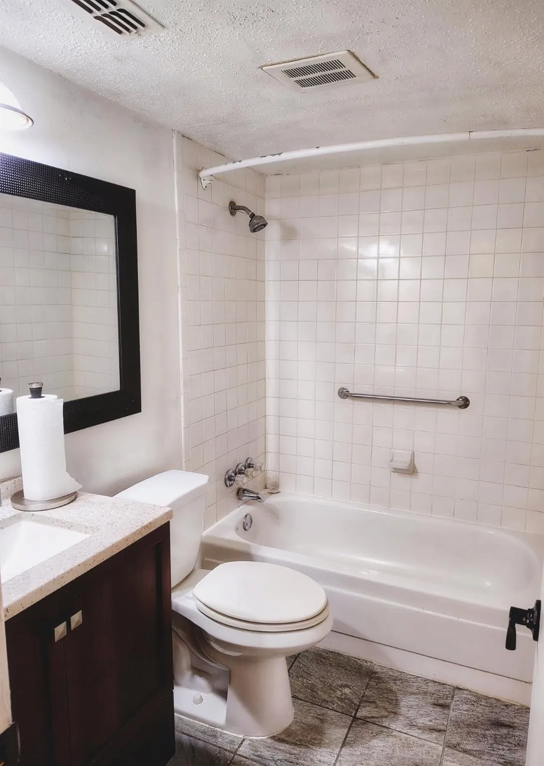 Bathroom featuring a shower/tub combination with white subway tile surround, dark wood-finish vanity with an integrated sink, and a framed mirror