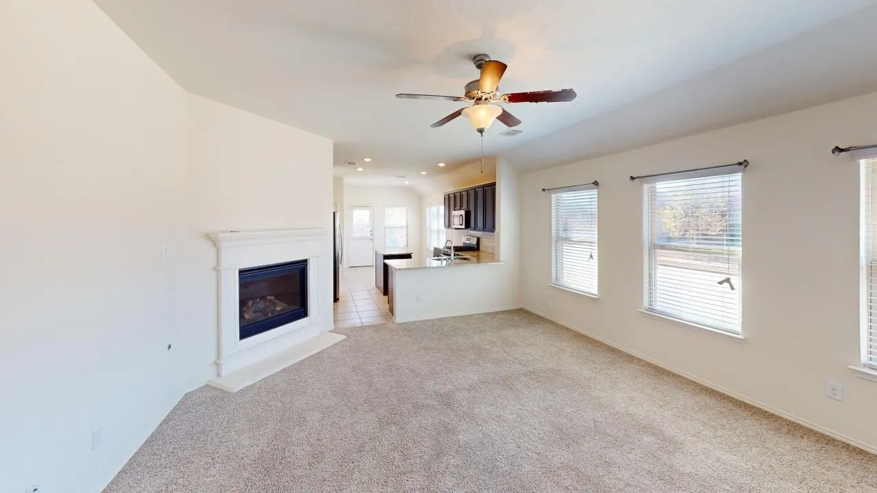 Living area featuring a fireplace with a mantel, ceiling fan with light fixture, multiple windows with blinds, and carpet flooring