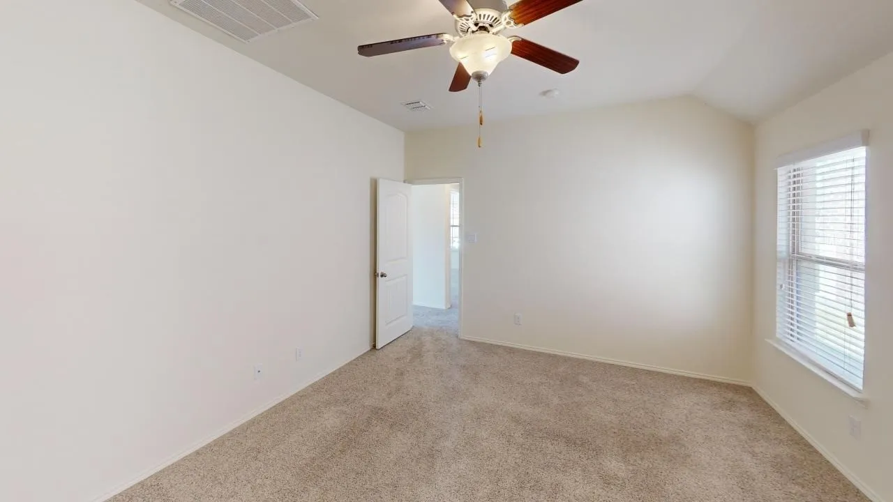 Carpeted interior with a ceiling fan, vaulted ceiling, and window with blinds