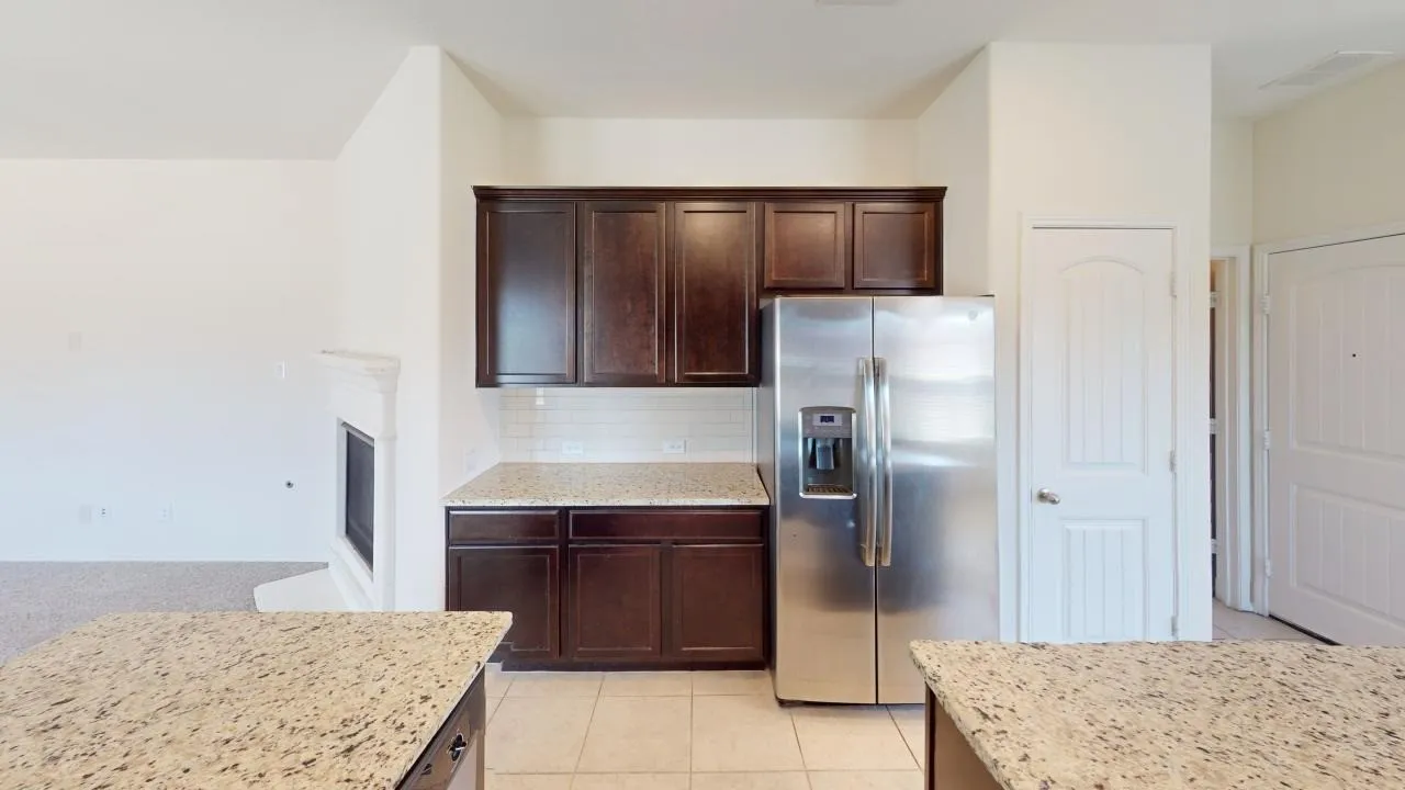 Stainless steel refrigerator with ice and water dispenser, dark wood-finish cabinetry, granite-style countertops, subway tile backsplash, and tile flooring