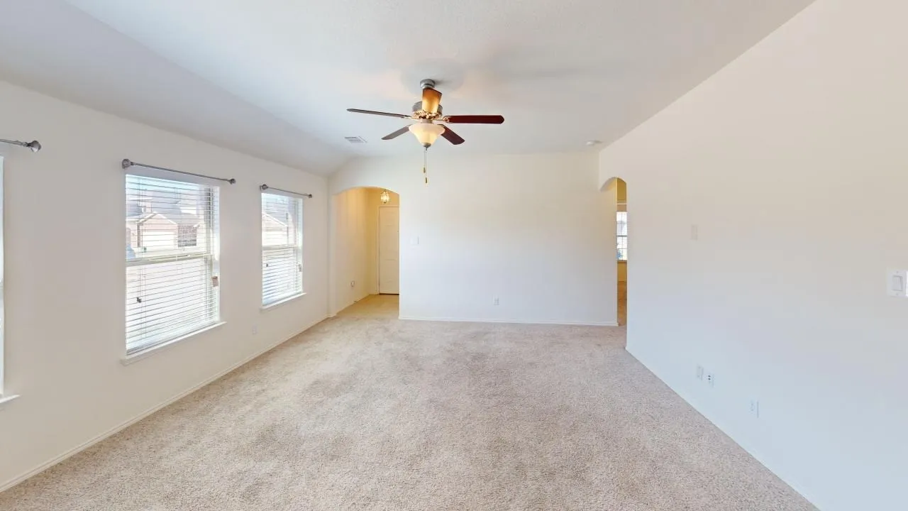 Expansive room featuring carpeted flooring, multiple windows with blinds, a ceiling fan with light fixture, and arched doorways