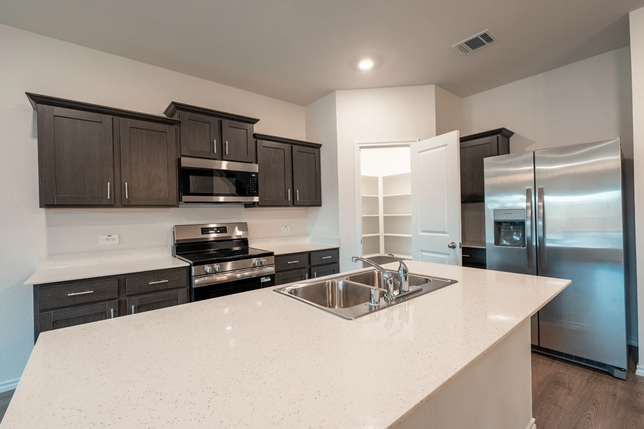 Modern open-concept kitchen featuring stainless steel appliances, sleek countertops, ample cabinetry, and upgraded decorative cabinet pulls, complemented by an upgraded dining light fixture. Large walk in pantry.