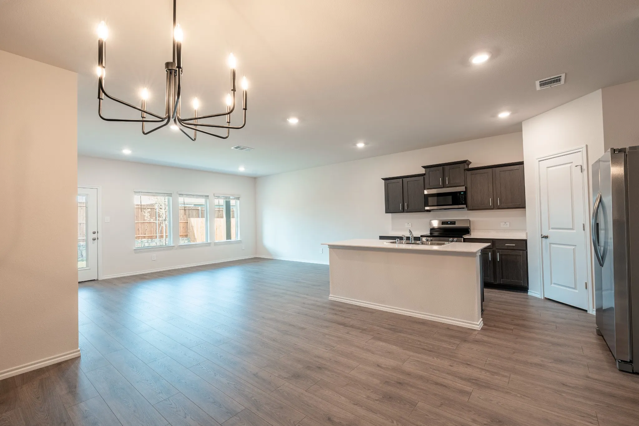 Modern open-concept kitchen featuring stainless steel appliances, sleek countertops, ample cabinetry, and upgraded decorative cabinet pulls, complemented by an upgraded dining light fixture.