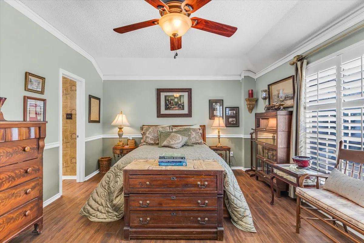 Wood-finish flooring, crown molding, ceiling fan with integrated lighting, and window with plantation shutters
