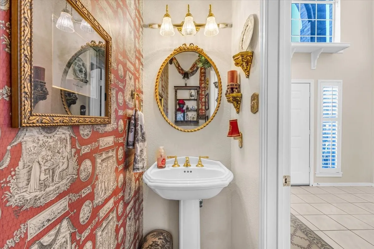 Pedestal sink with brass-finish faucet, framed mirror, and wall-mounted lighting