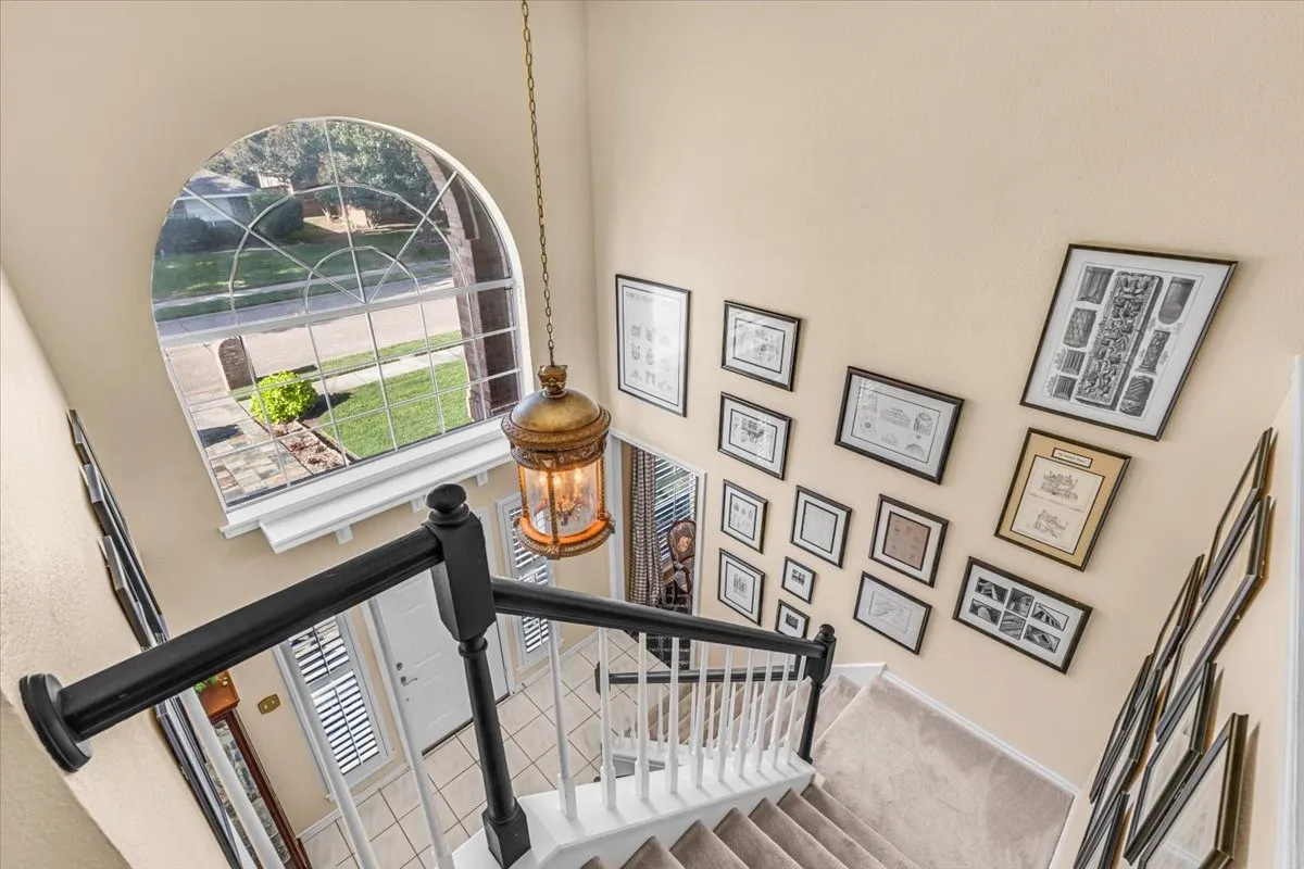 Arched window with decorative grilles, carpeted staircase with white risers, black handrail and balusters, and a suspended lantern fixture
