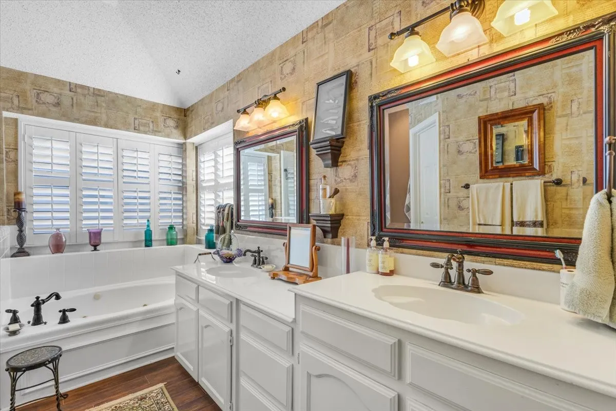 Jetted soaking tub with plantation shutters, dual vanities with integrated sinks, and individual framed mirrors