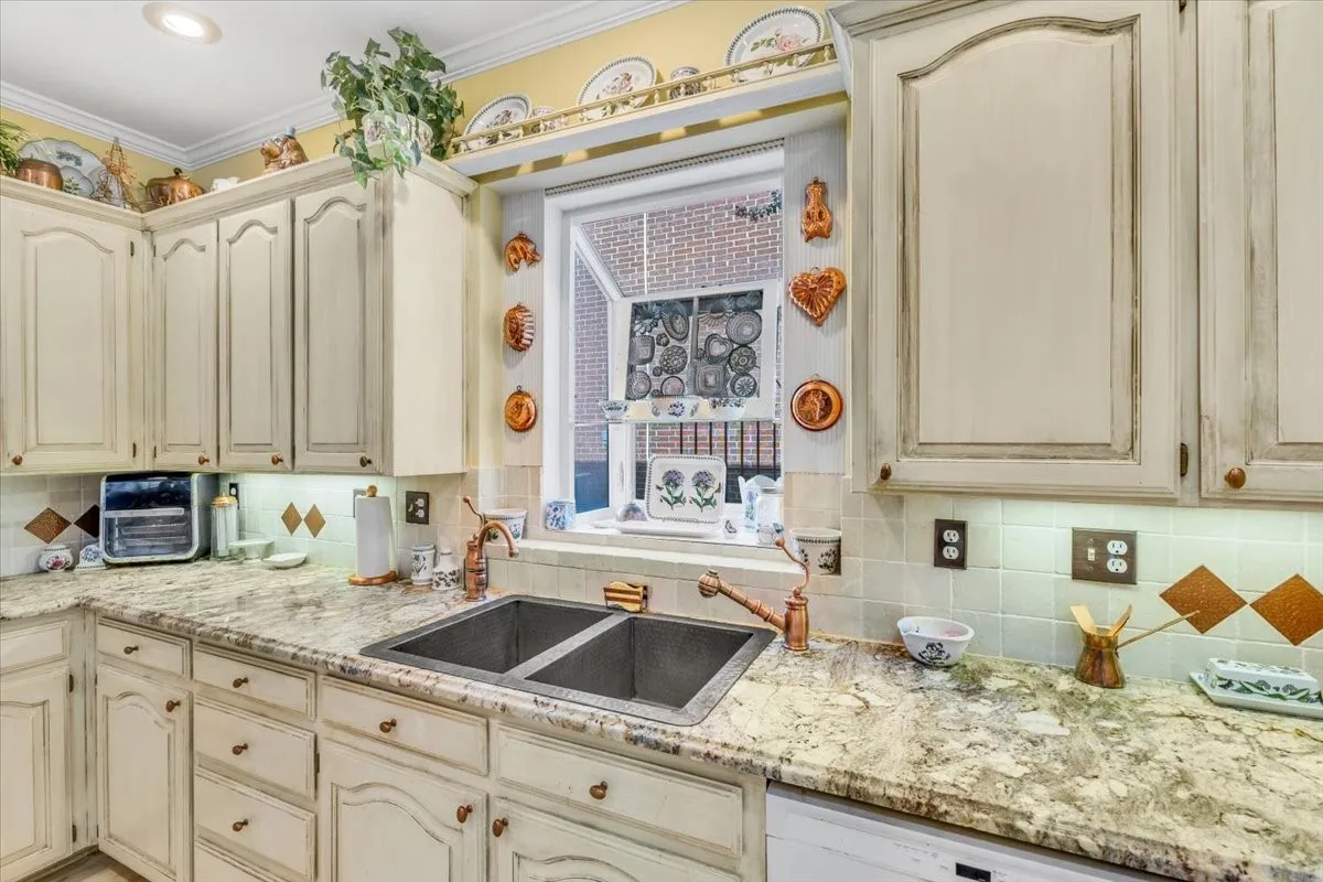 Light-toned cabinetry with decorative hardware, granite-look countertops, undermount double-basin sink, and a tile backsplash with decorative accents