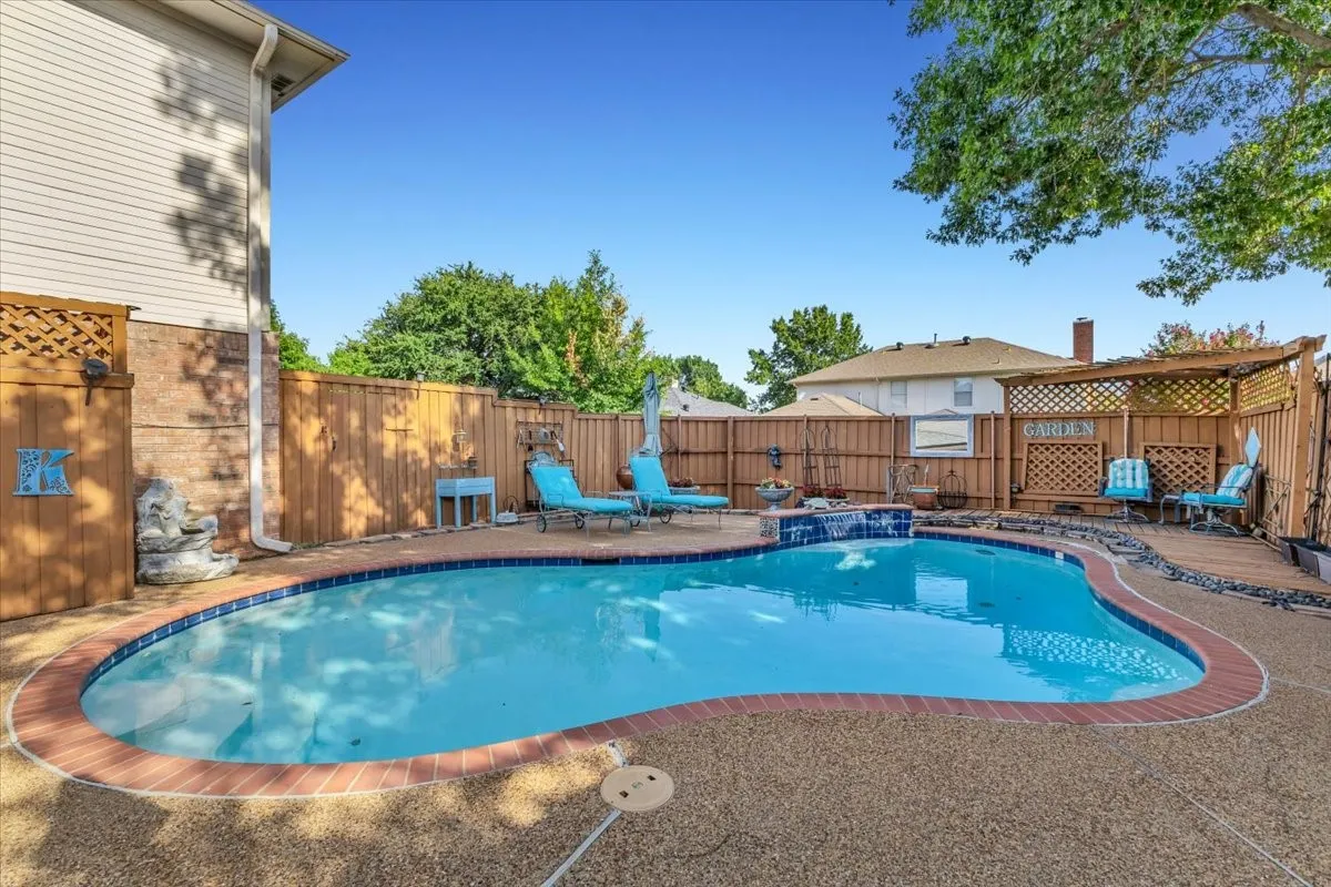 Freeform swimming pool with a stone aggregate deck, brick coping, and a waterfall feature