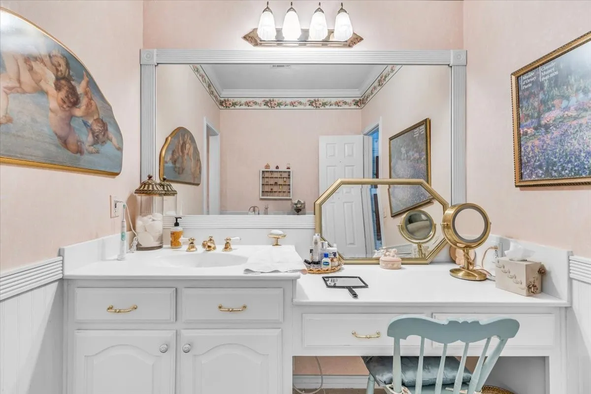 White vanity with integrated sink, brass fixtures, large wall-mounted mirror, and dedicated makeup area