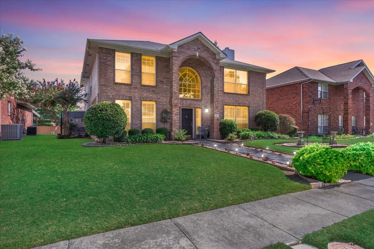 Brick exterior with arched window, established landscaping, walkway lighting, and a well-maintained lawn