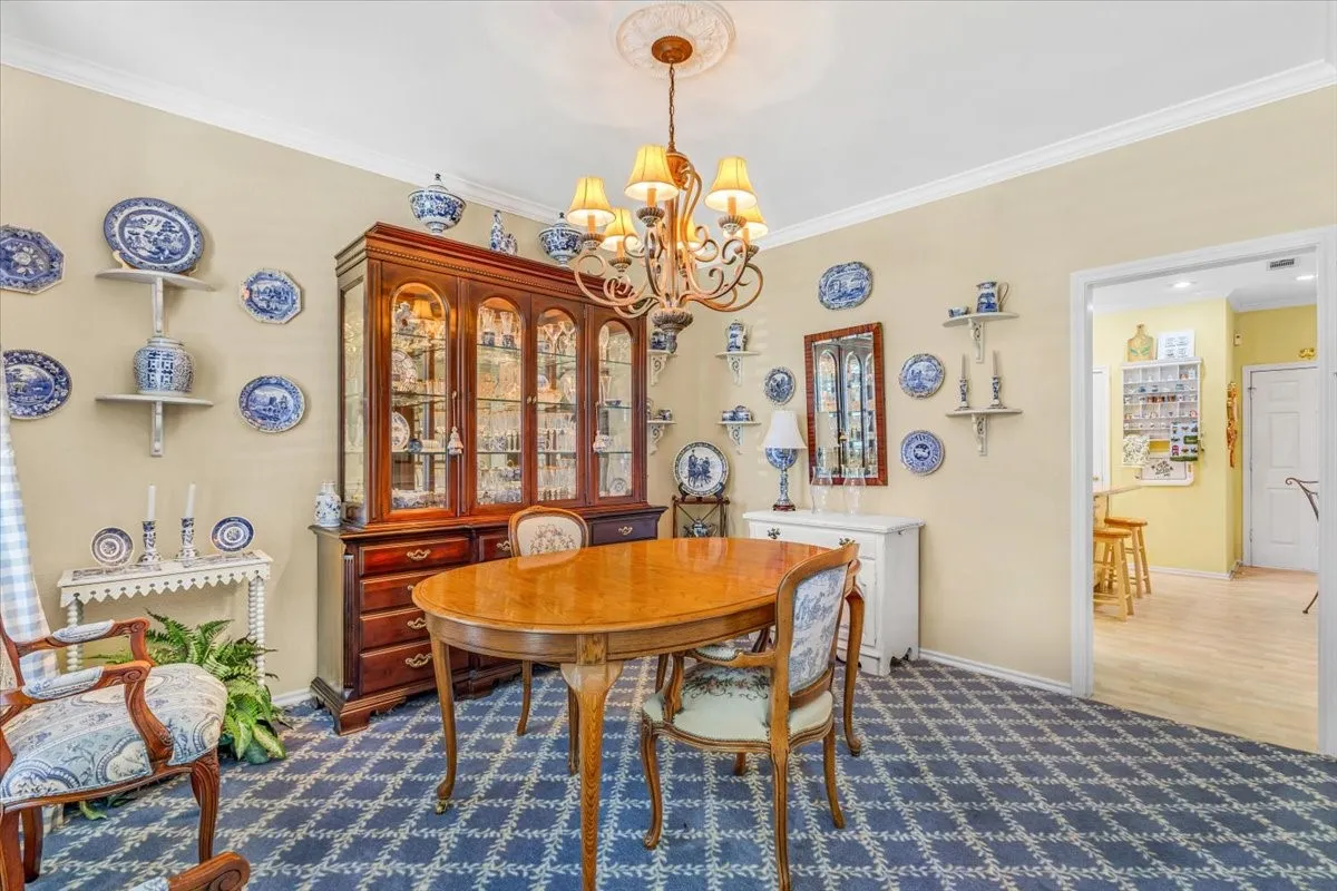 Crown molding, decorative ceiling medallion, patterned carpeting, recessed lighting within built-in cabinetry, and a doorway with light wood-finish flooring visible beyond