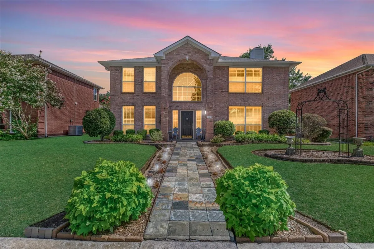 Brick exterior with arched main entrance, stone-paved walkway with integrated lighting, manicured lawn, and established landscaping