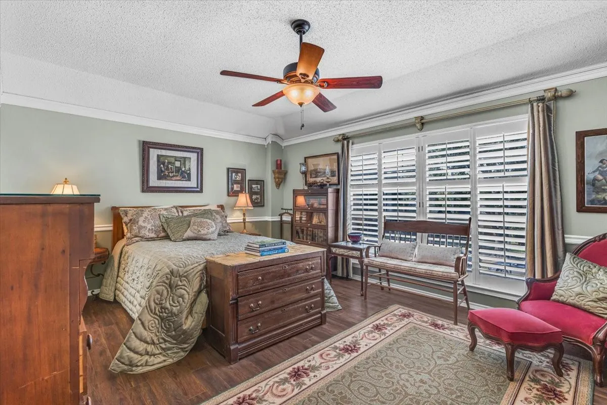 Wood-finish flooring, crown molding, ceiling fan, and white plantation shutters