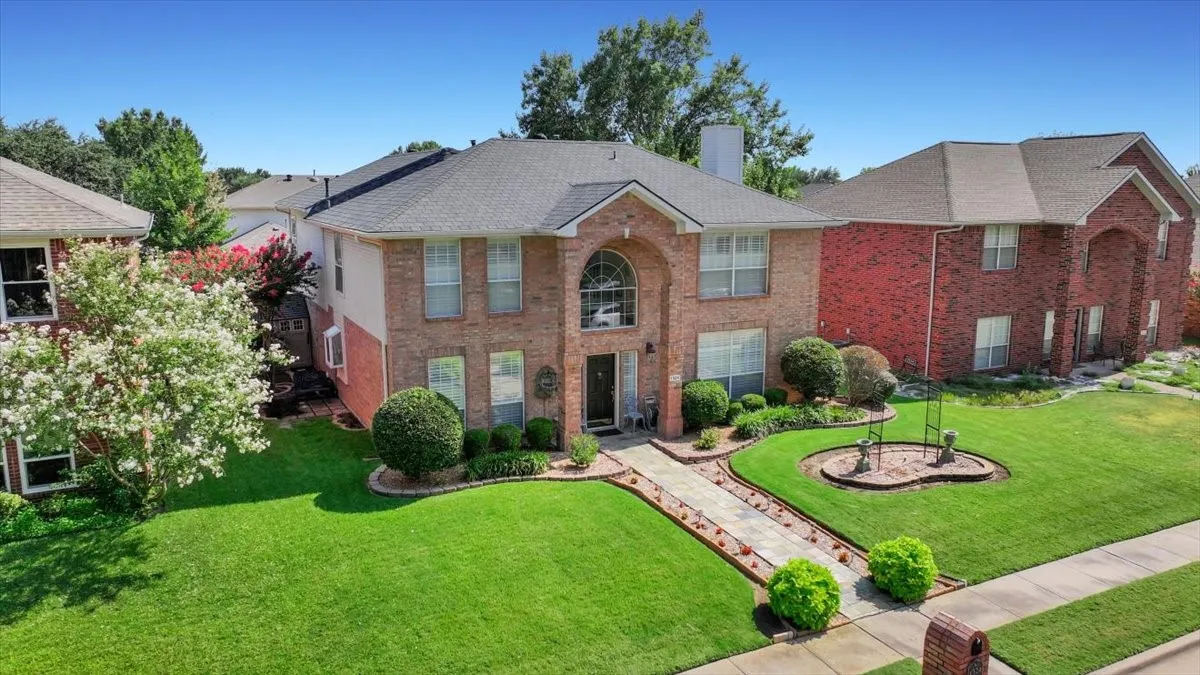 Brick exterior with an arched entry, mature landscaping, paved walkway, and a prominent chimney