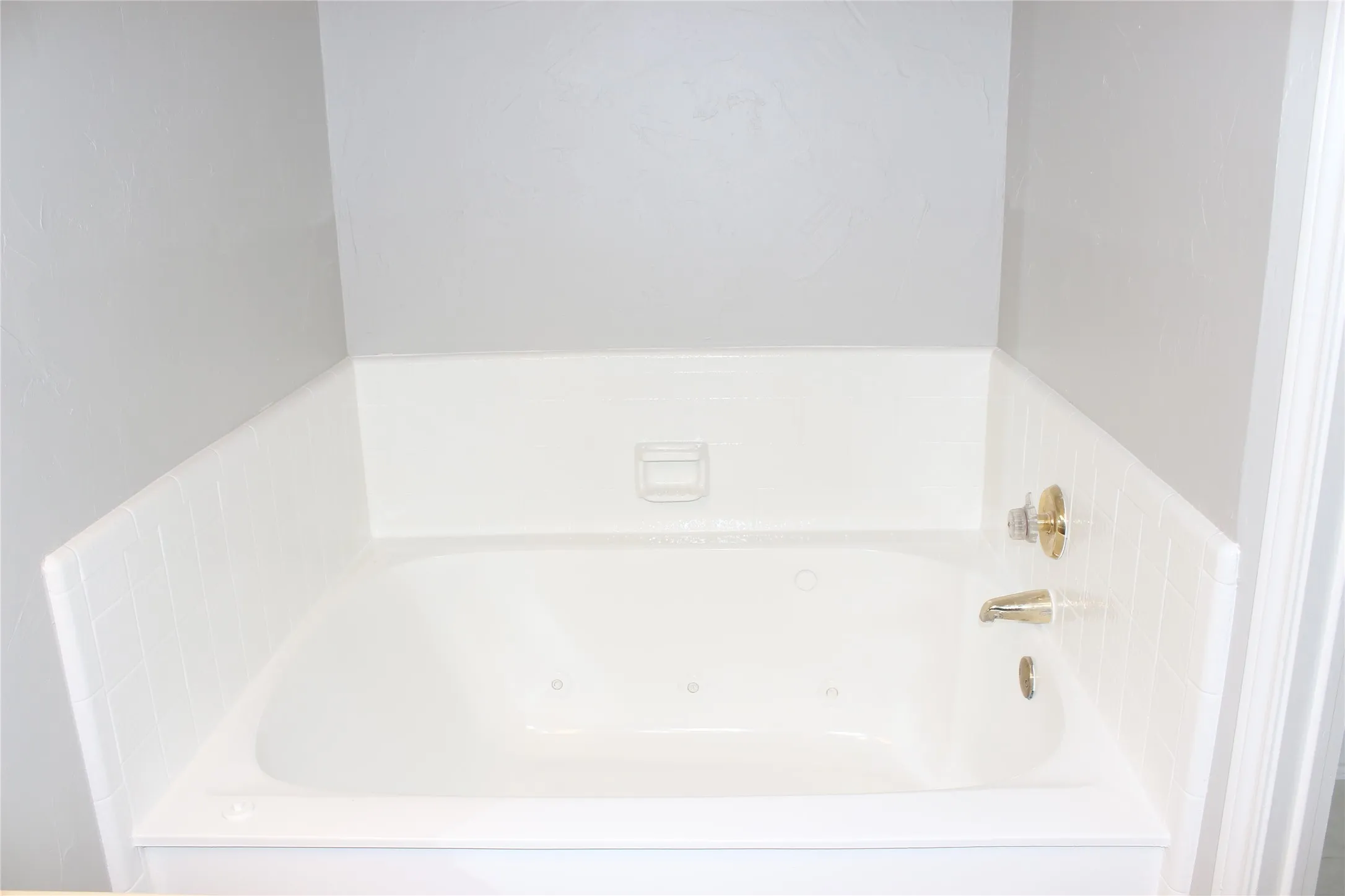Soaking tub featuring integrated jets, white tile surround, and polished brass fixtures