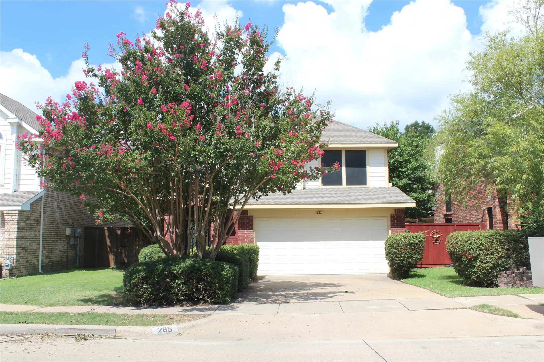 Two-story residence featuring a prominent flowering tree, brick facade accents, and light-colored siding