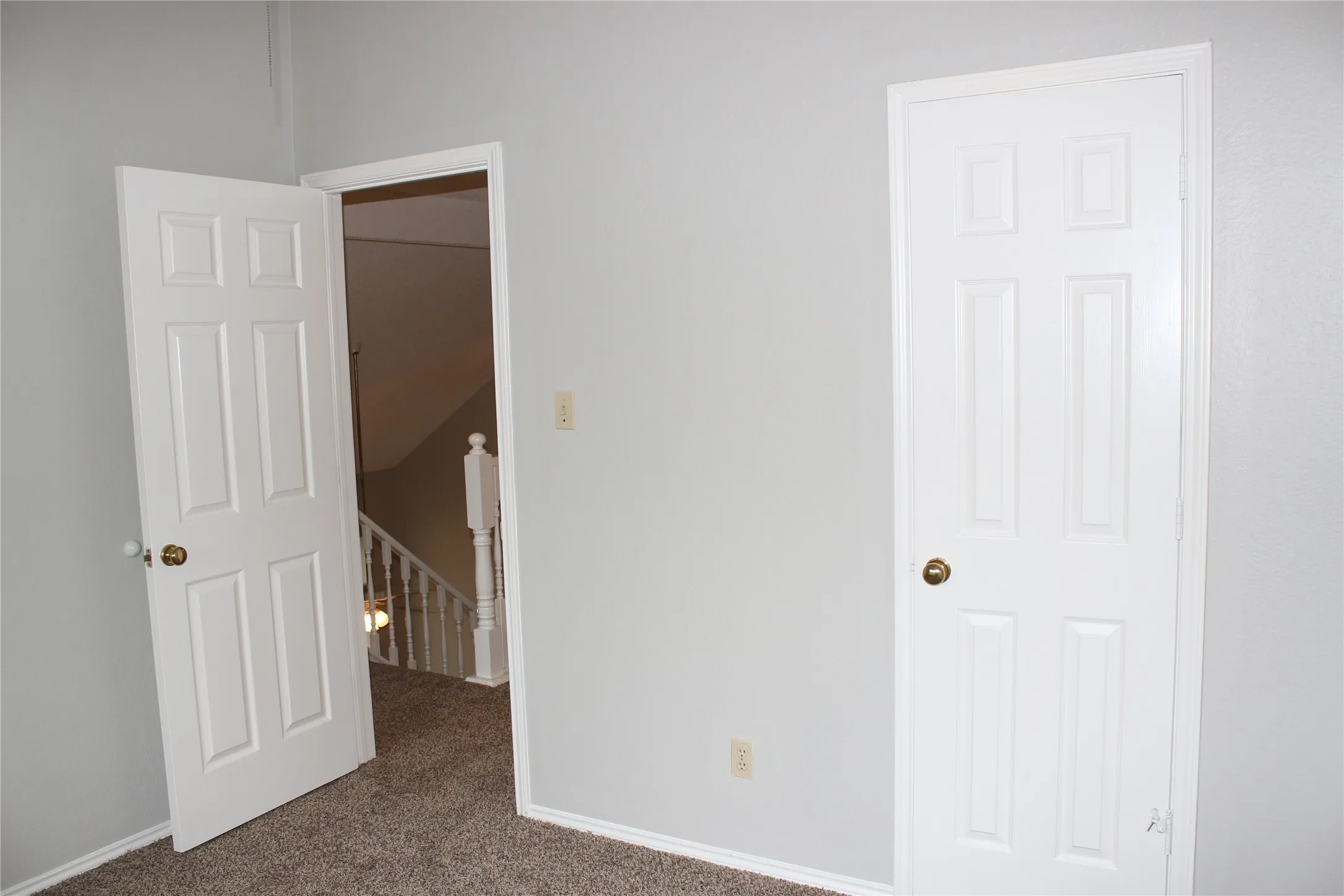 Interior space featuring light gray walls, textured carpeting, and white trim