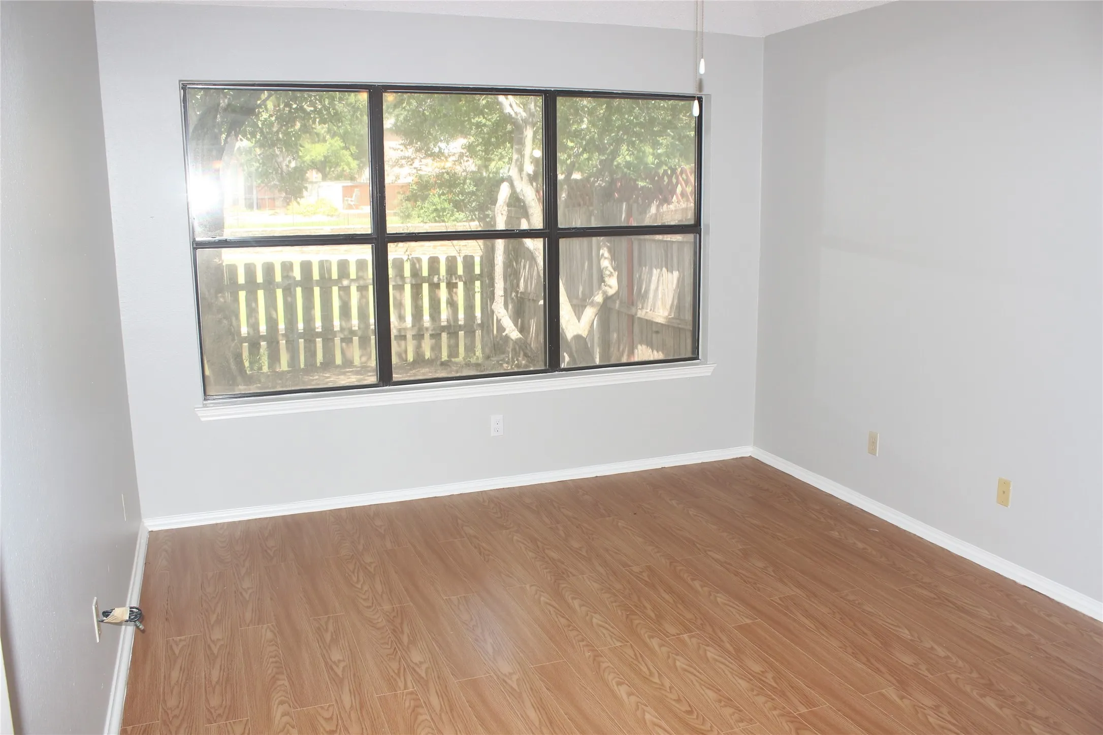 Spacious room featuring wood-finish flooring, light gray wall paint, and white baseboards