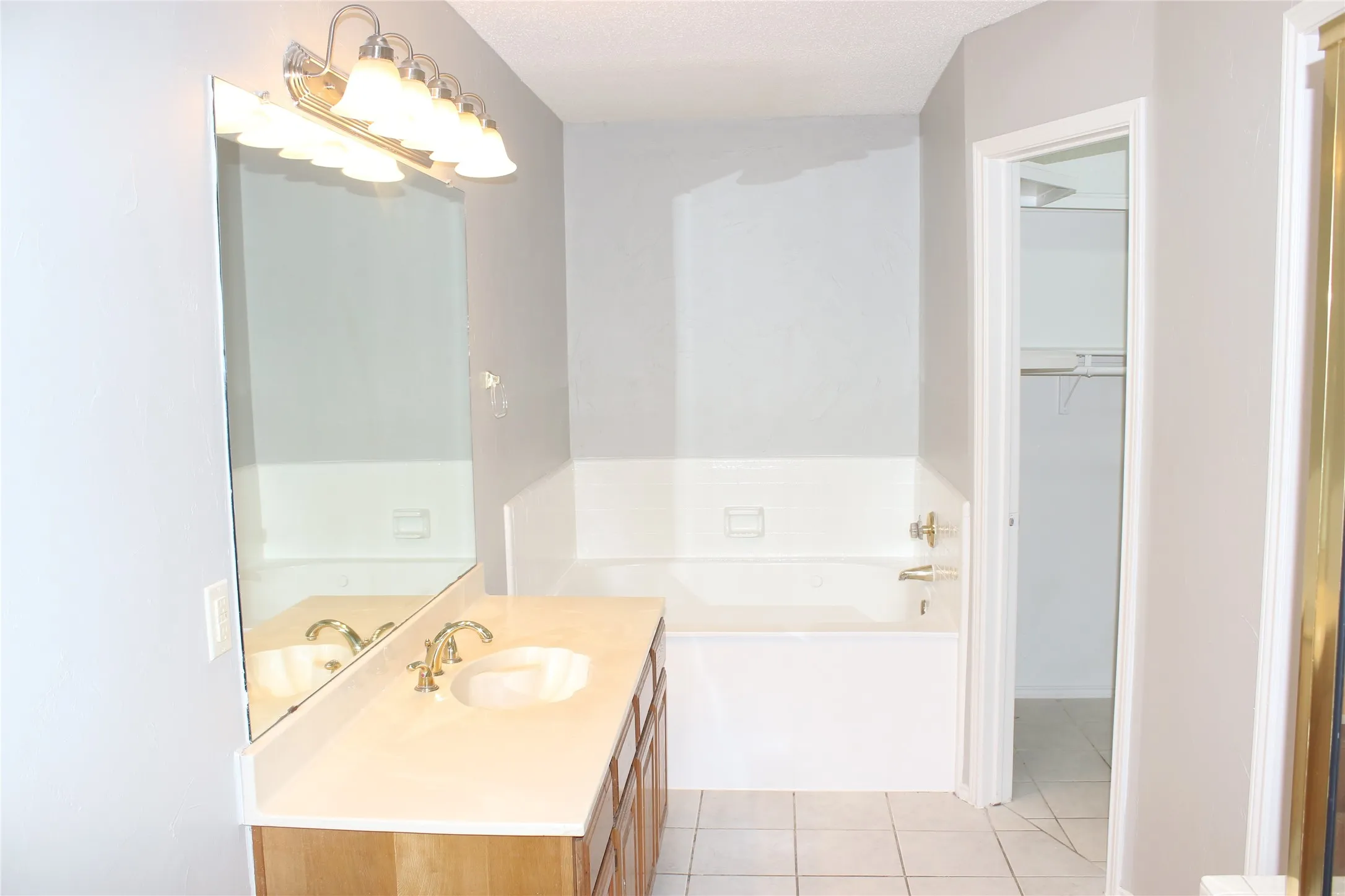 Bathroom featuring a wood-finish vanity with a single sink, an integrated bathtub, and tiled flooring