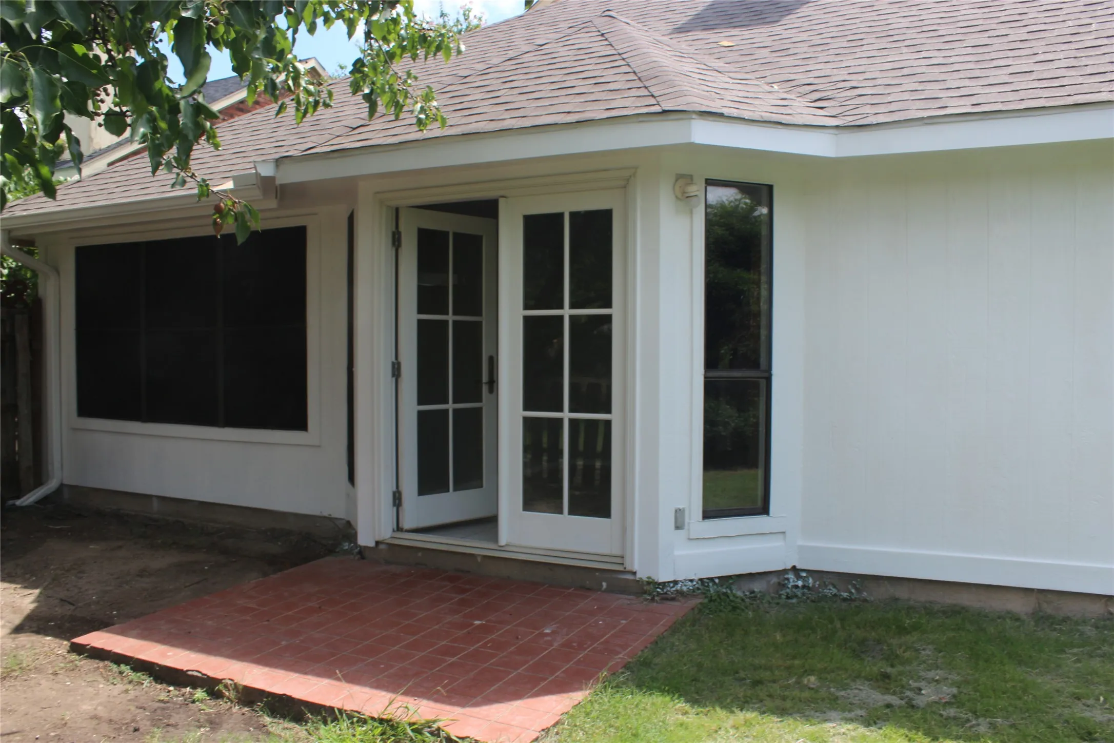Exterior featuring French doors, a screened window, a vertical window, white siding, and a partial shingle roof