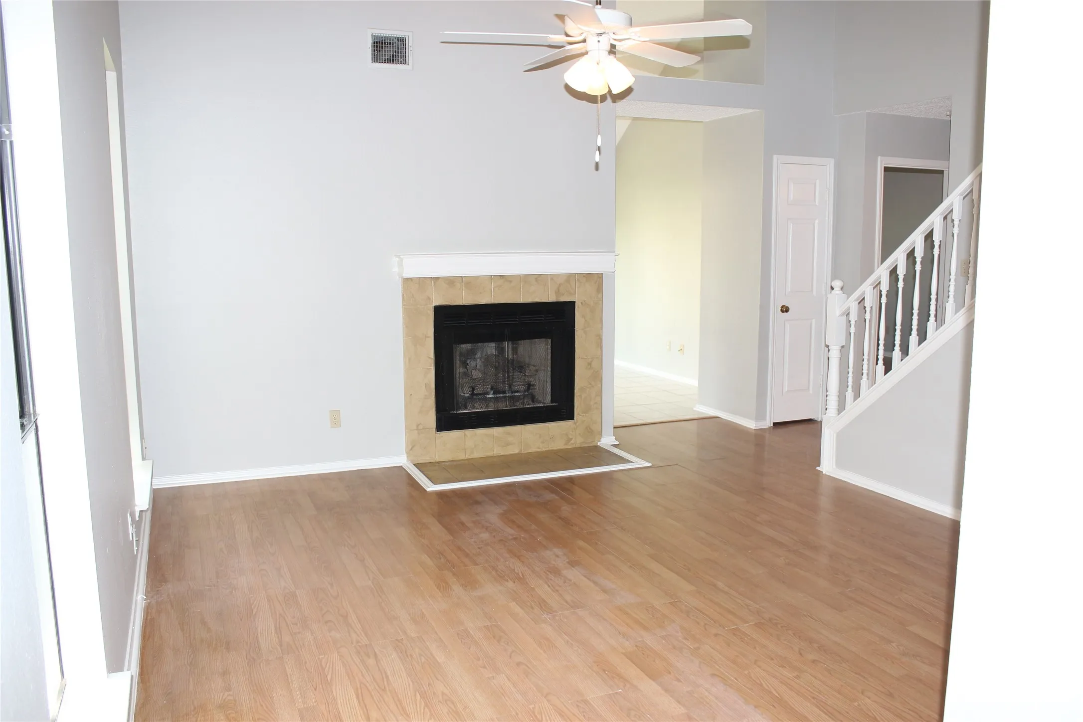 Living area featuring wood-finish flooring, a fireplace with a tiled surround and hearth, a ceiling fan, and painted walls