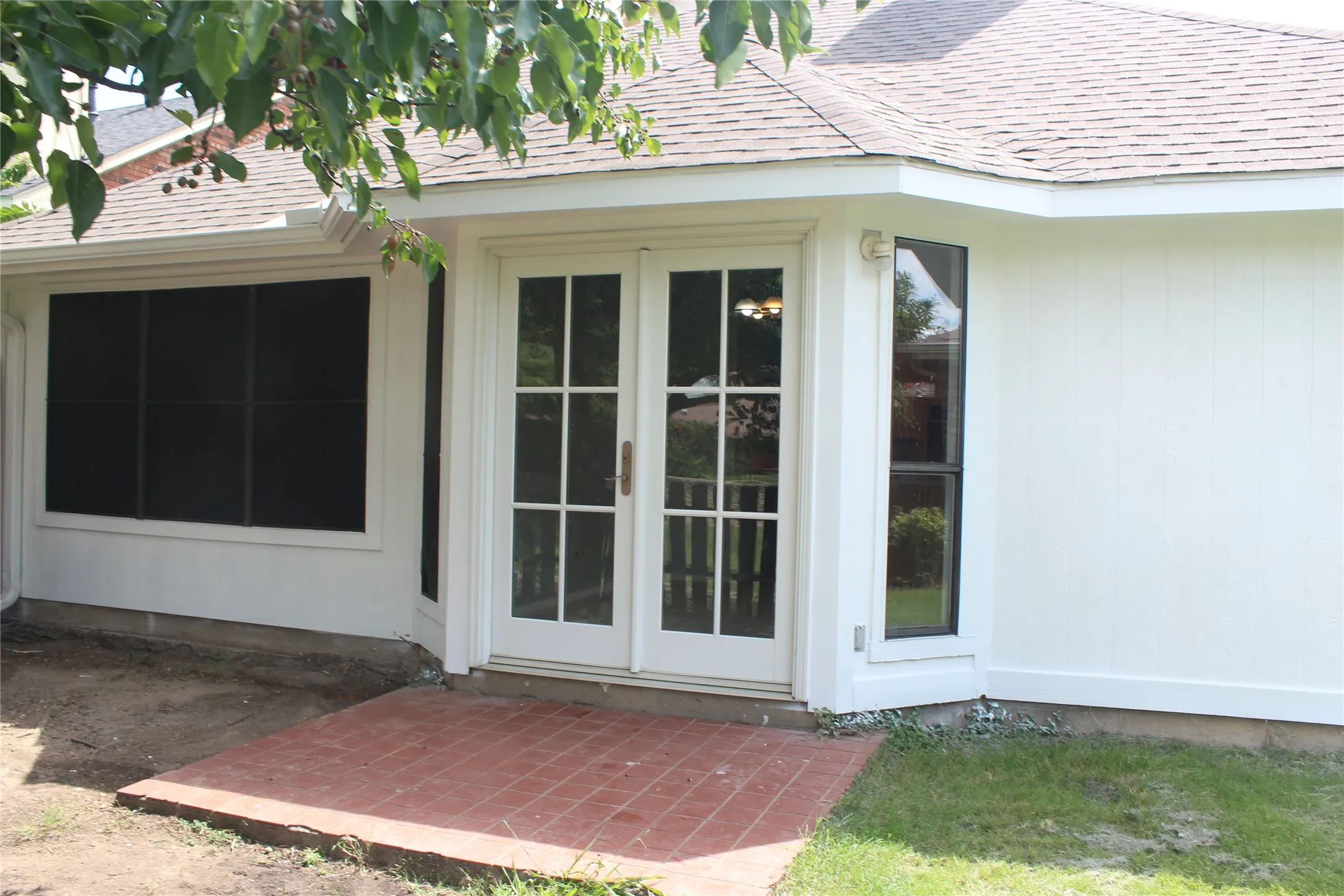 Exterior white siding featuring a bay window with a tall, narrow pane, a large window with black screening, and glass French doors