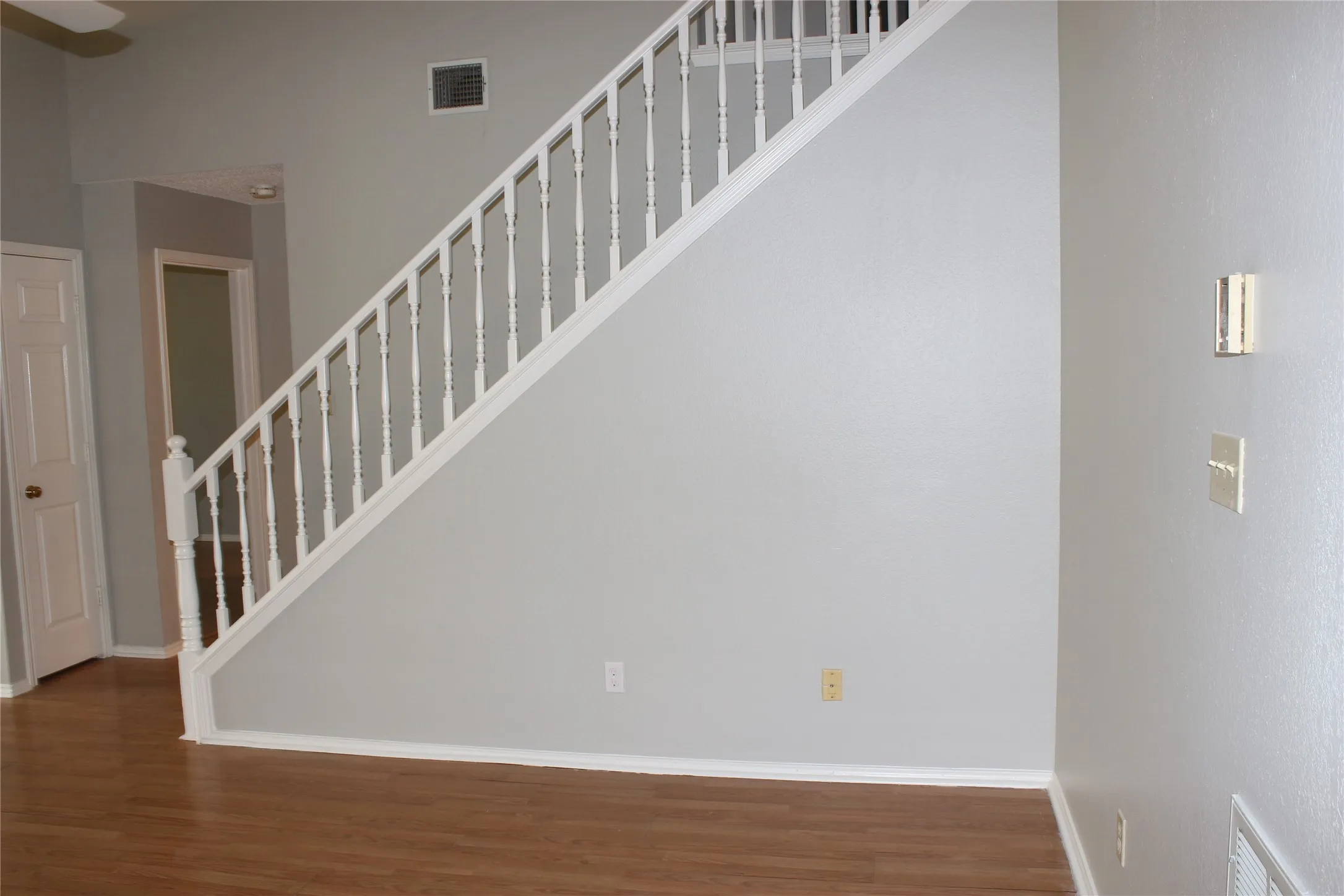 Staircase featuring white balusters and handrail, gray wall paint, wood-finish flooring, and white baseboards