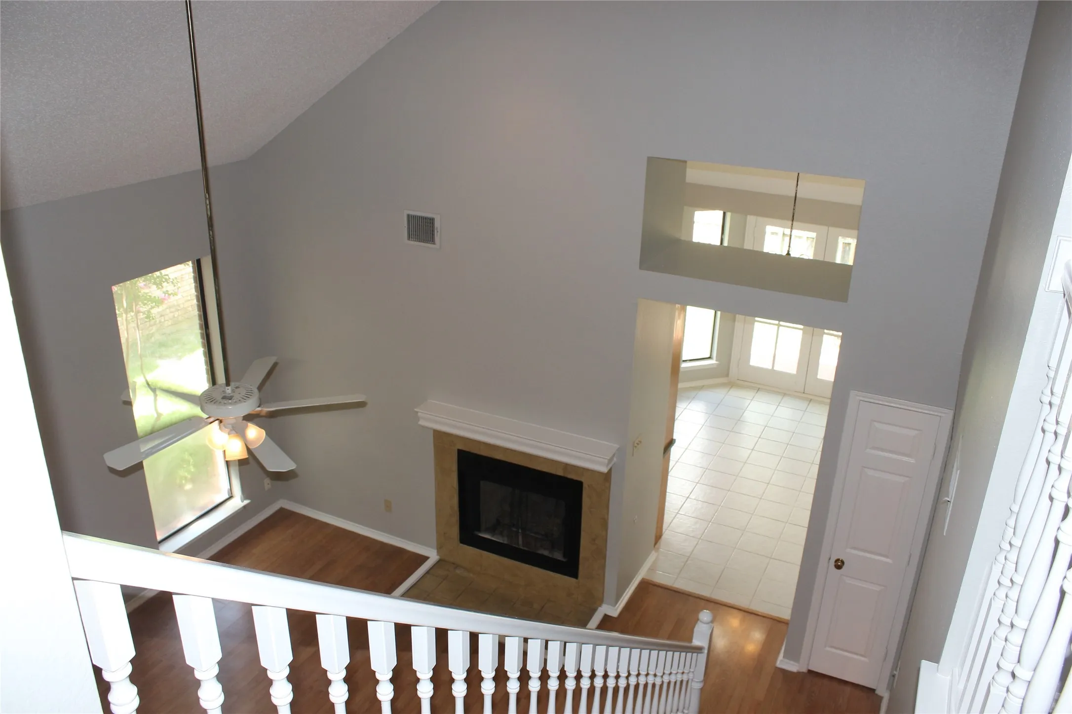 Two-story living area with vaulted ceilings and a ceiling fan, featuring a fireplace with a stone surround and mantel