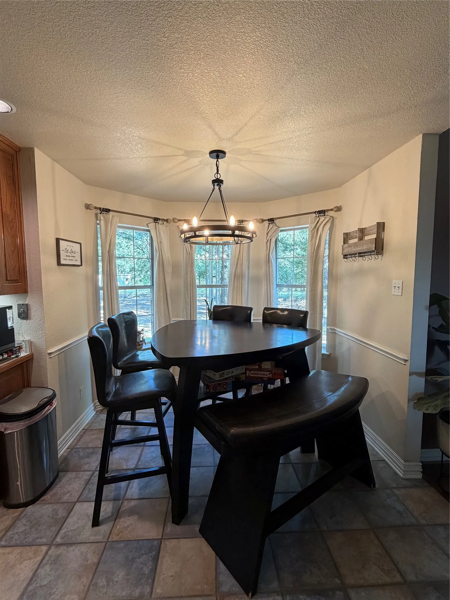 Bay window with three large windows, wainscoting, a modern chandelier, and tile flooring