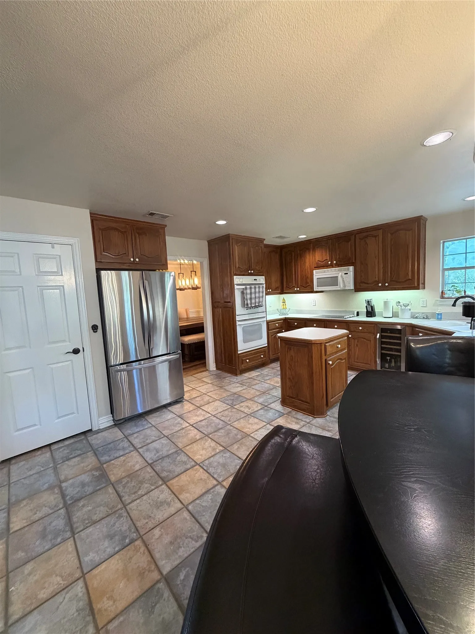 Kitchen featuring wood cabinetry, tile flooring, recessed lighting, and a kitchen island.  Stainless fridge, dishwasher, and wine fridge.