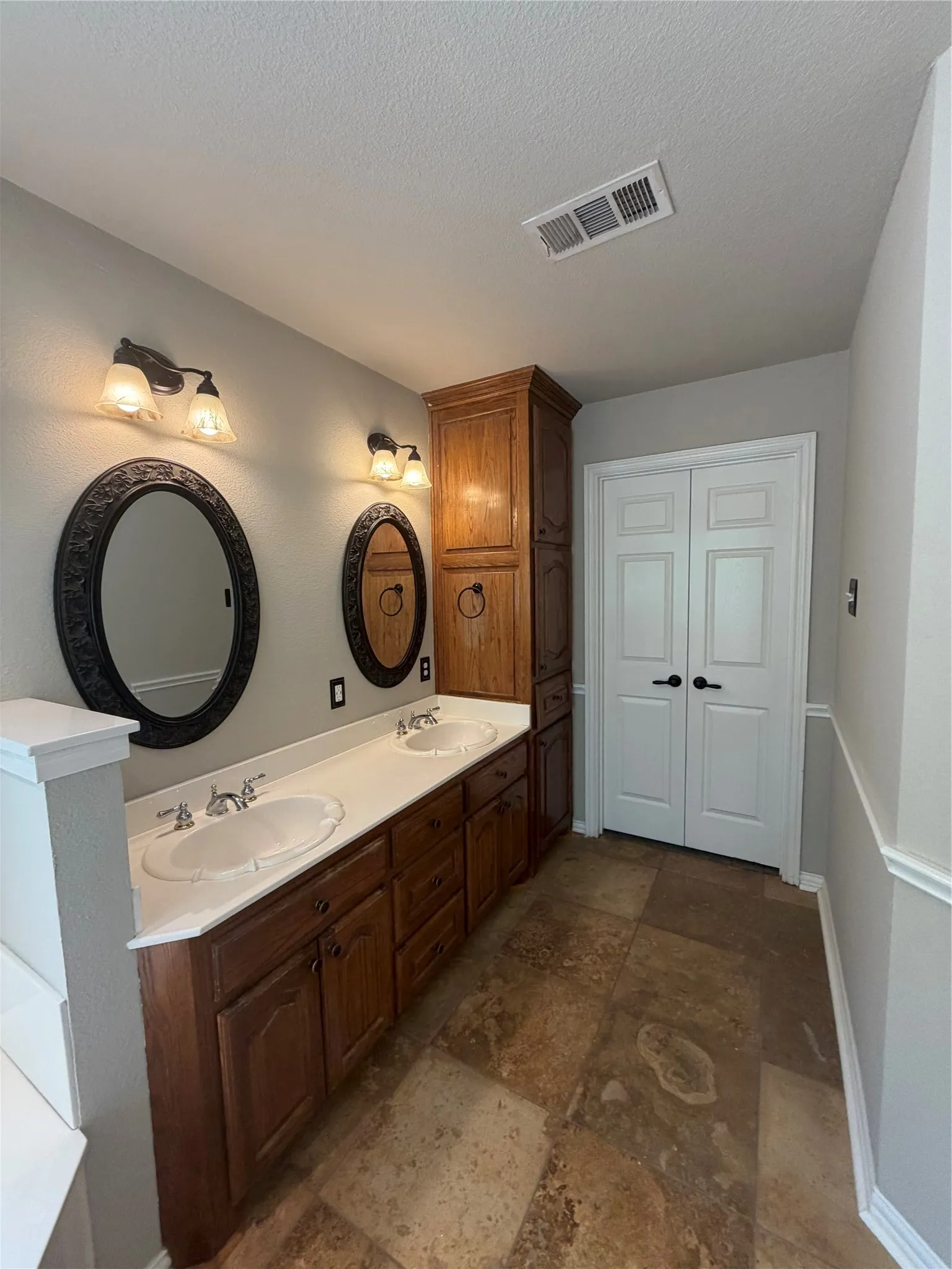 Master Bath. Double vanity with integrated sinks, wood cabinetry, built-in storage cabinet, oval mirrors, and tile flooring