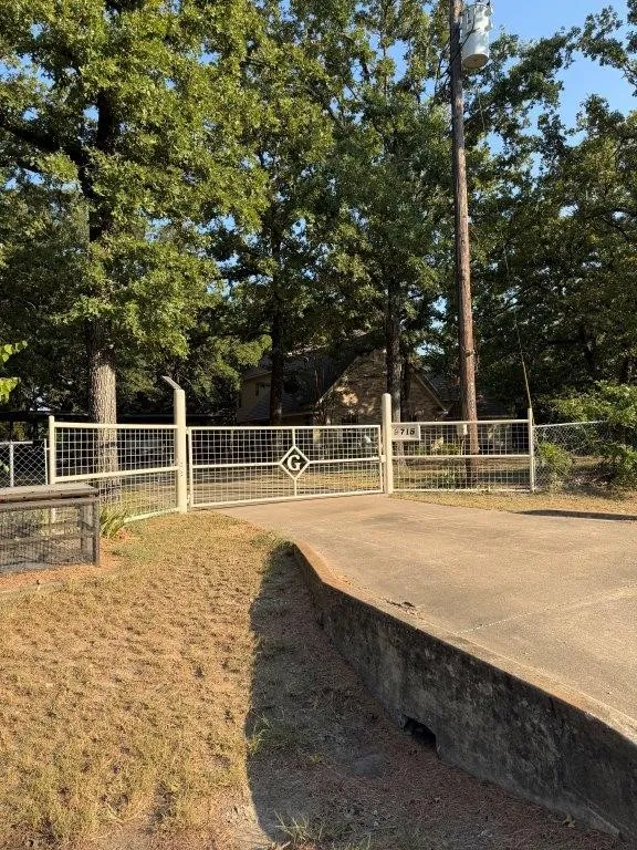Gated entry with a concrete driveway, surrounded by mature trees