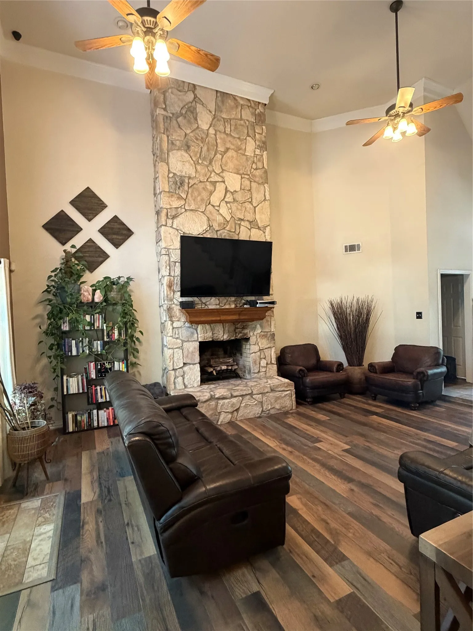 Vaulted ceilings with crown molding, stone-clad fireplace, wood-finish flooring, and built-in ceiling fans