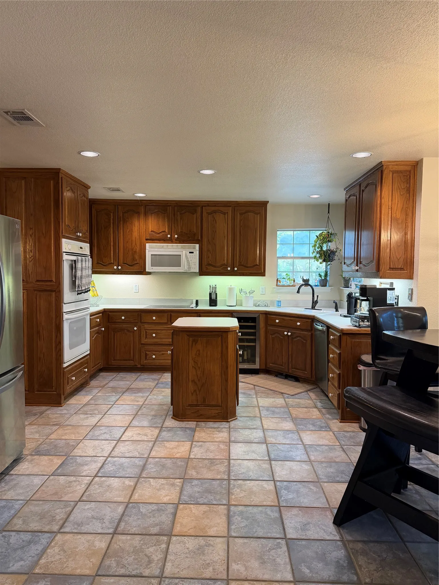 Spacious kitchen featuring rich wood cabinetry, light countertops, built-in double ovens, a central island, and tiled flooring