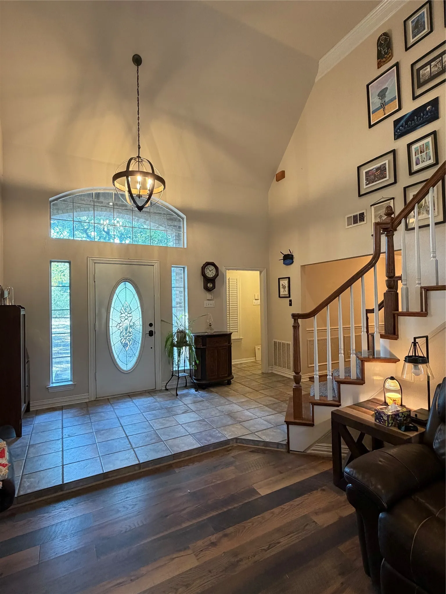 Vaulted ceiling with an modern chandelier, decorative entry door with sidelights, transom window, tile flooring, and wood-finish flooring